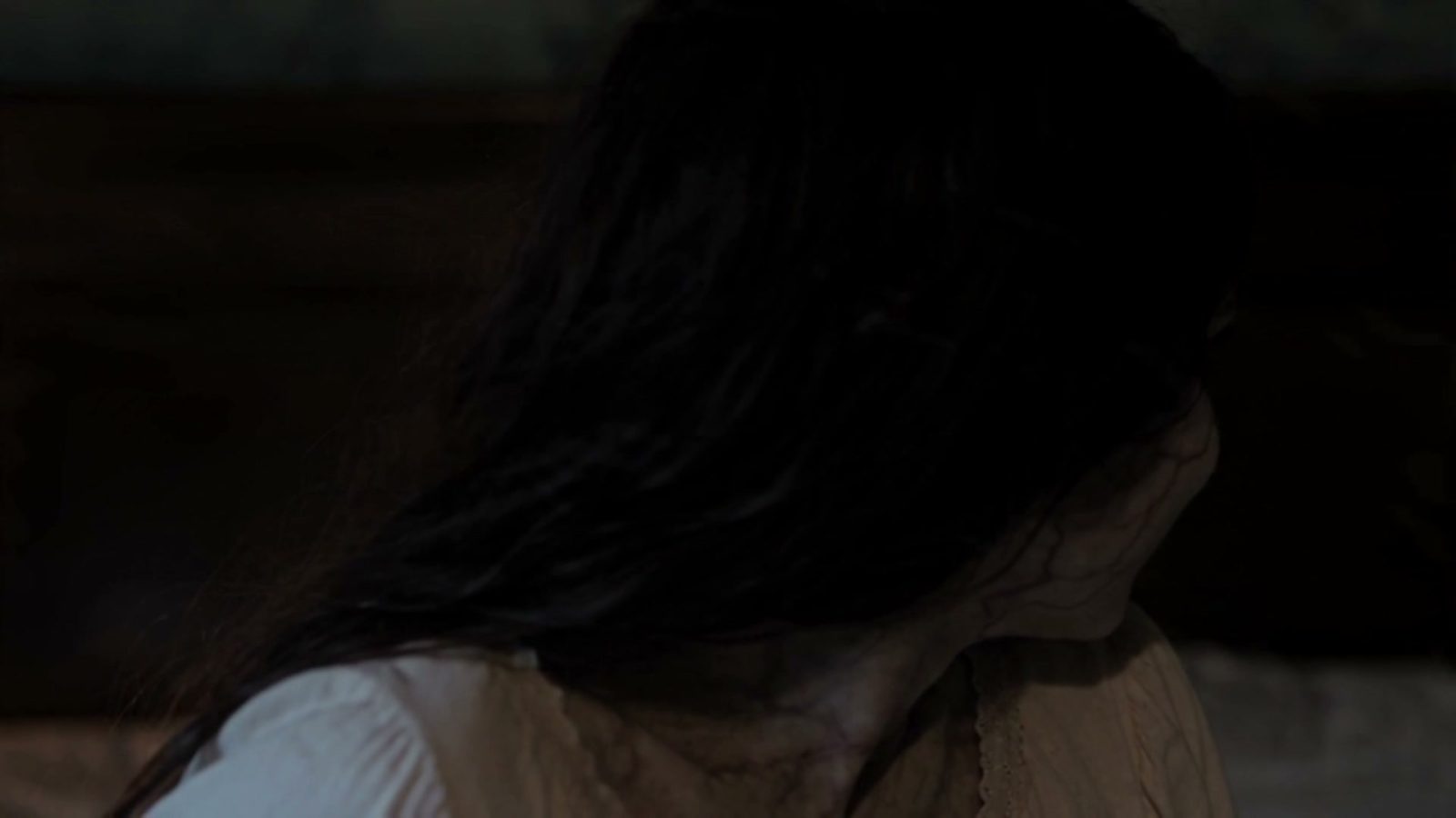 La possédée de dos, cheveux devant le visage, la chambre presque noire