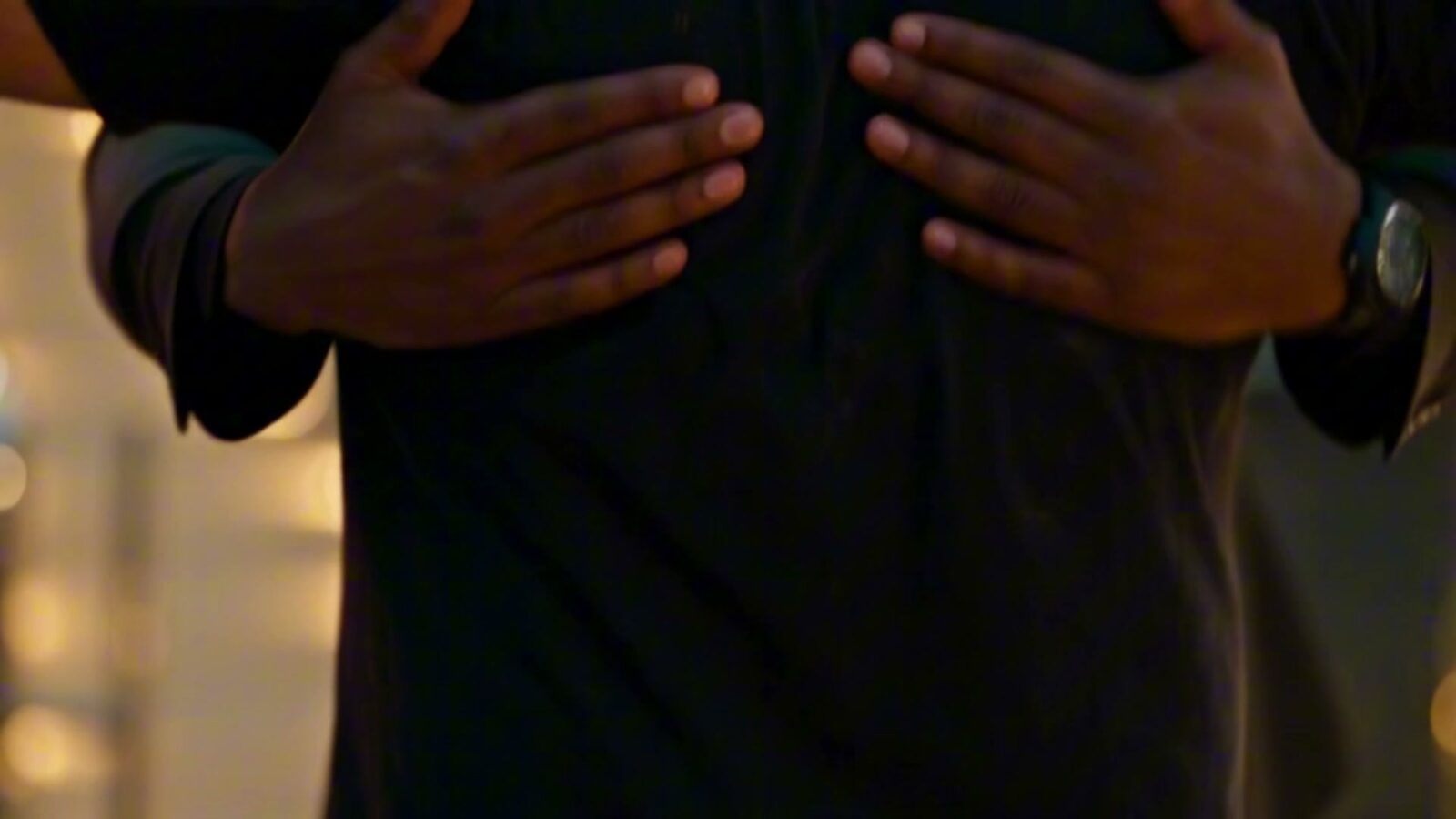 Plan de détail : deux mains fouillent le tee-shirt déchiré de l'homme traqué