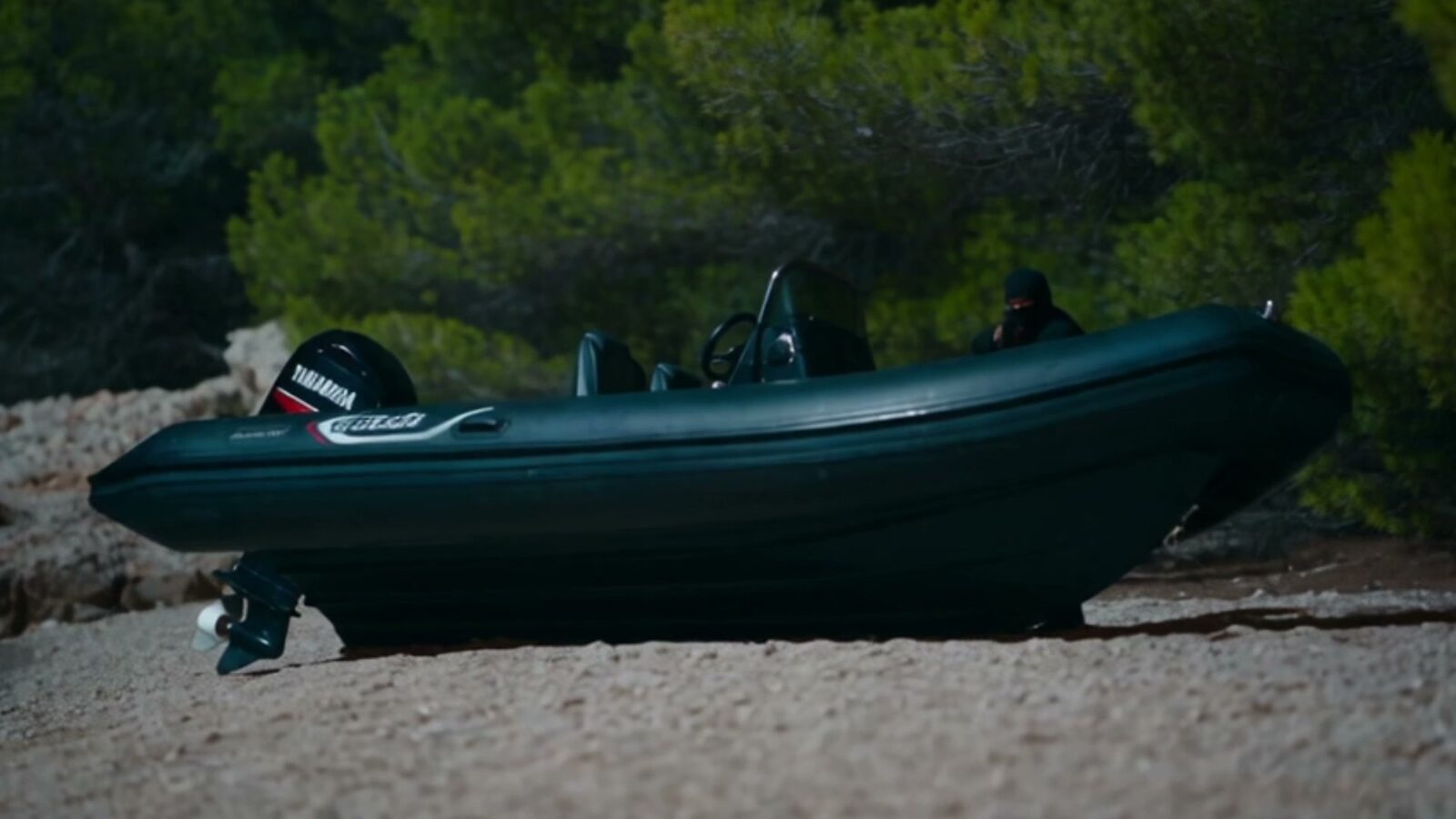 Le pneumatique échoué sur une plage de galets, un homme en noir toujours à bord