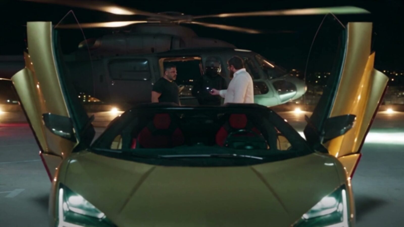 La Lamborghini dorée portes ouvertes devant un hélicoptère, trois hommes discutent sur l'hélisurface