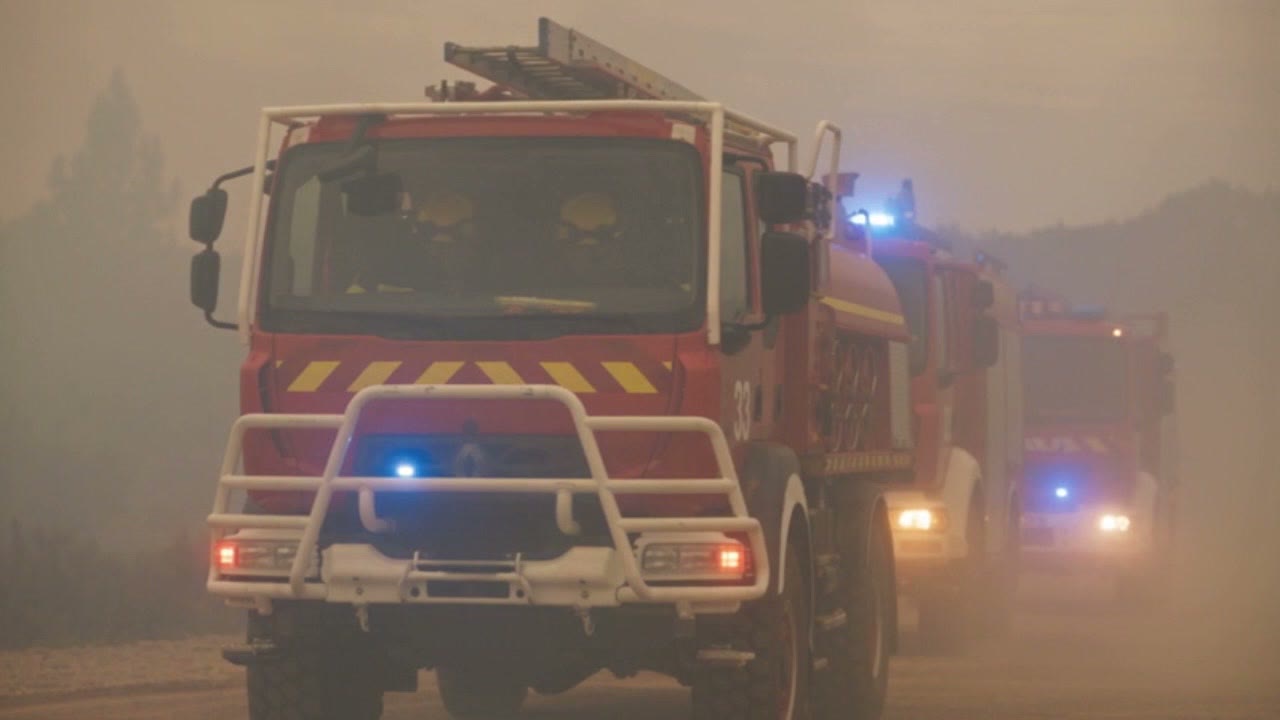 Un camion de pompiers gyrophares allumés avance dans la fumée