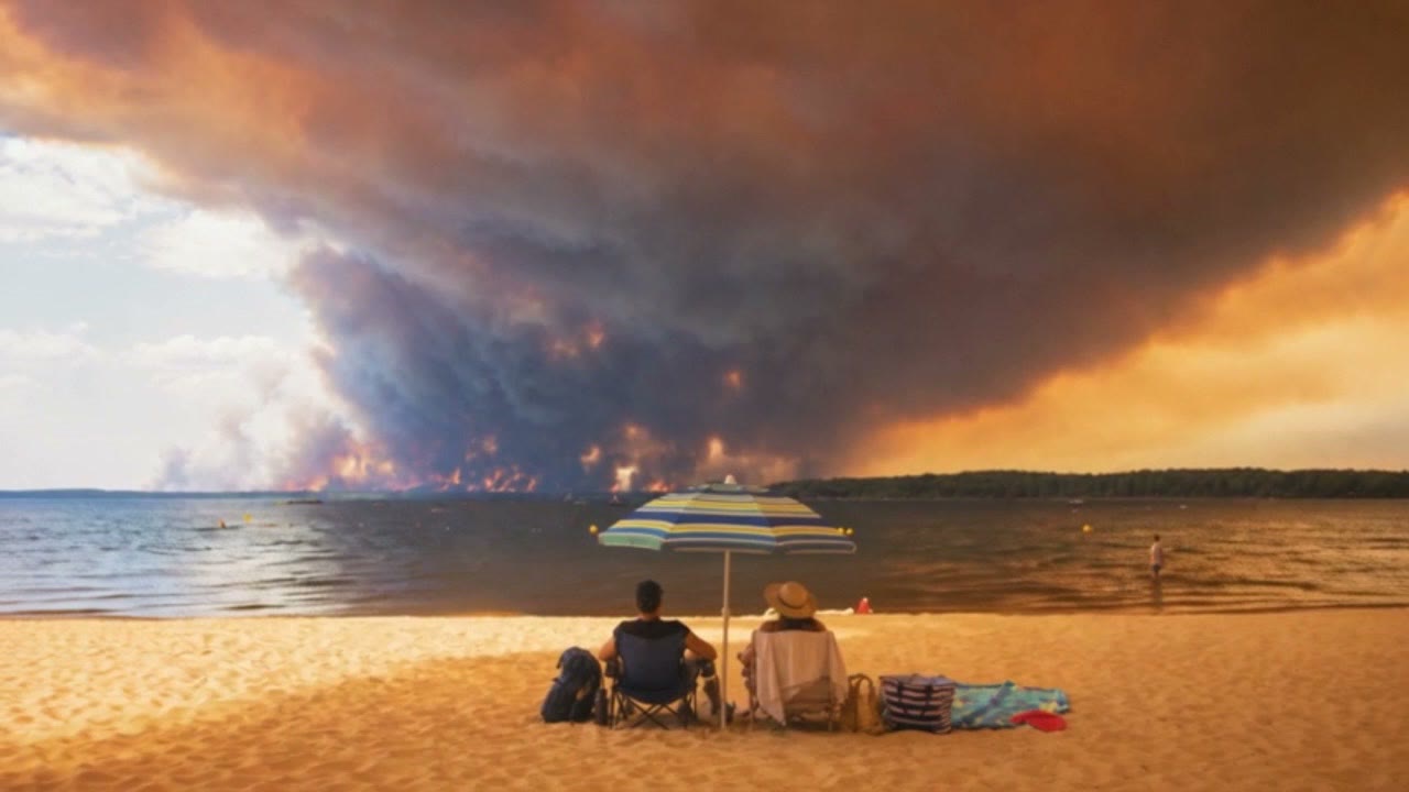 Des vacanciers sur la plage face à un immense panache de fumée à l'horizon