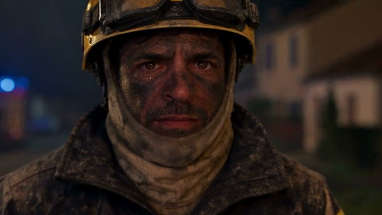 Portrait d'un pompier épuisé devant une maison sauvée des flammes