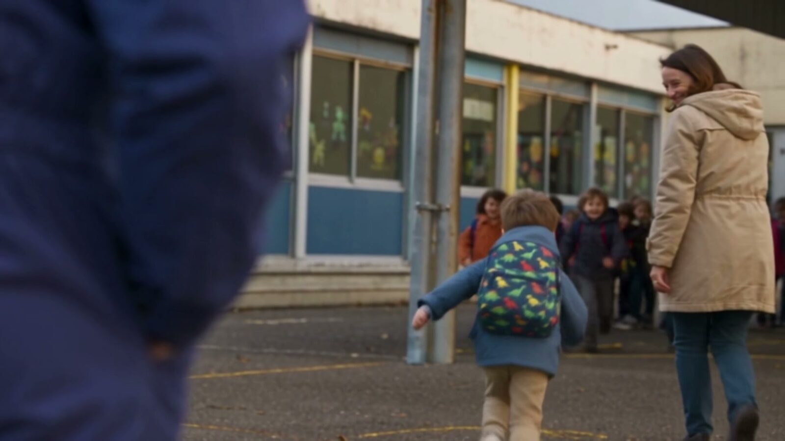 Devant l'école, le garçon court vers l'entrée, cartable sur le dos