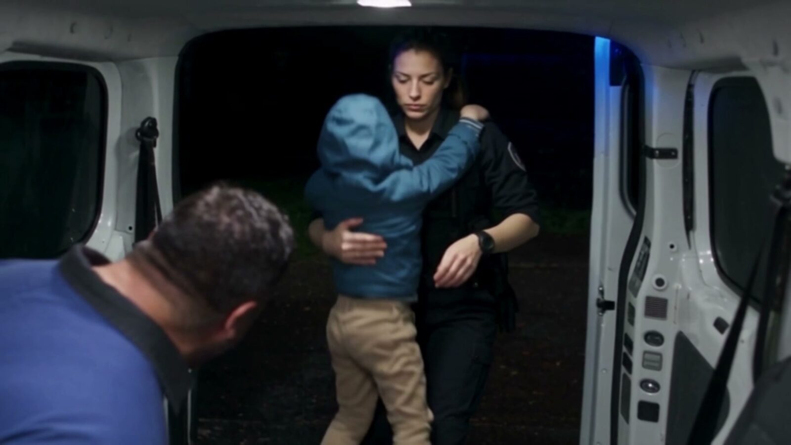 La nuit, une policière porte l'enfant jusqu'au fourgon sous le regard du père