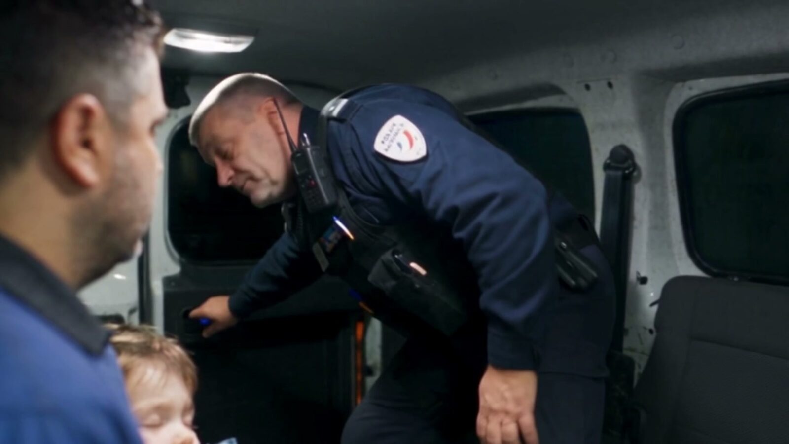 Un policier se penche dans le fourgon pour parler au père et à son fils