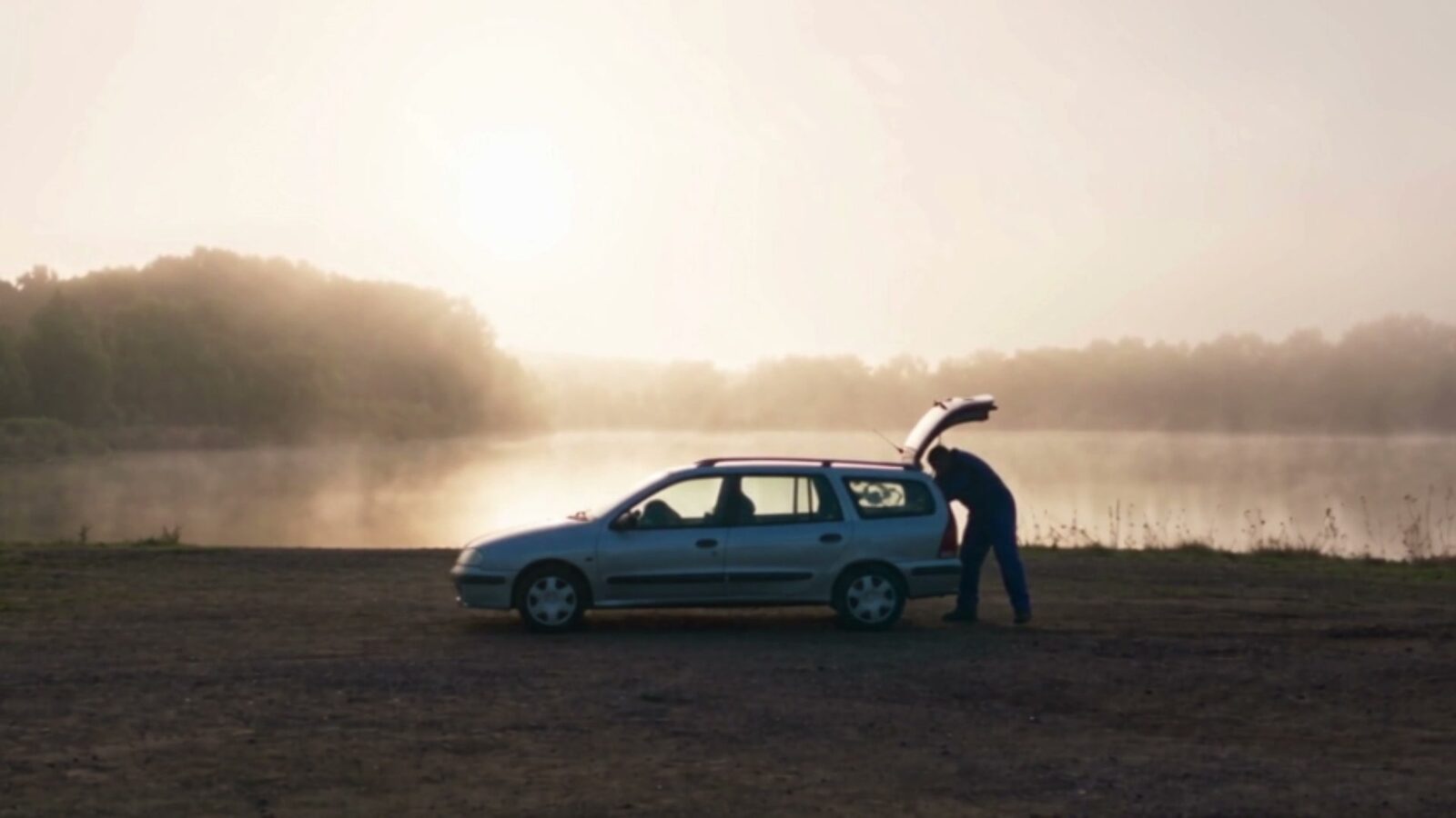 Le lac à l'aube dans la brume, la voiture du père garée sur la rive, coffre ouvert