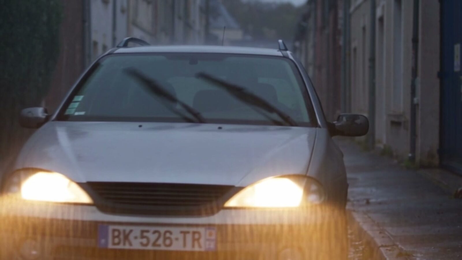 La voiture du père, phares allumés, sous la pluie