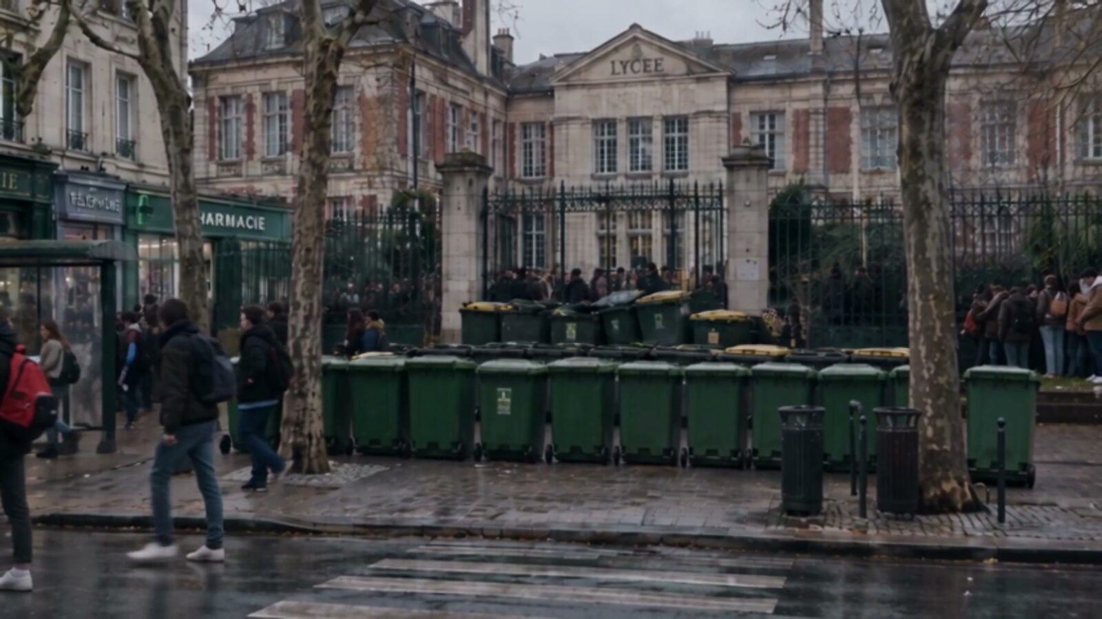 Devant les grilles du lycée, une barricade de poubelles vertes barre la rue