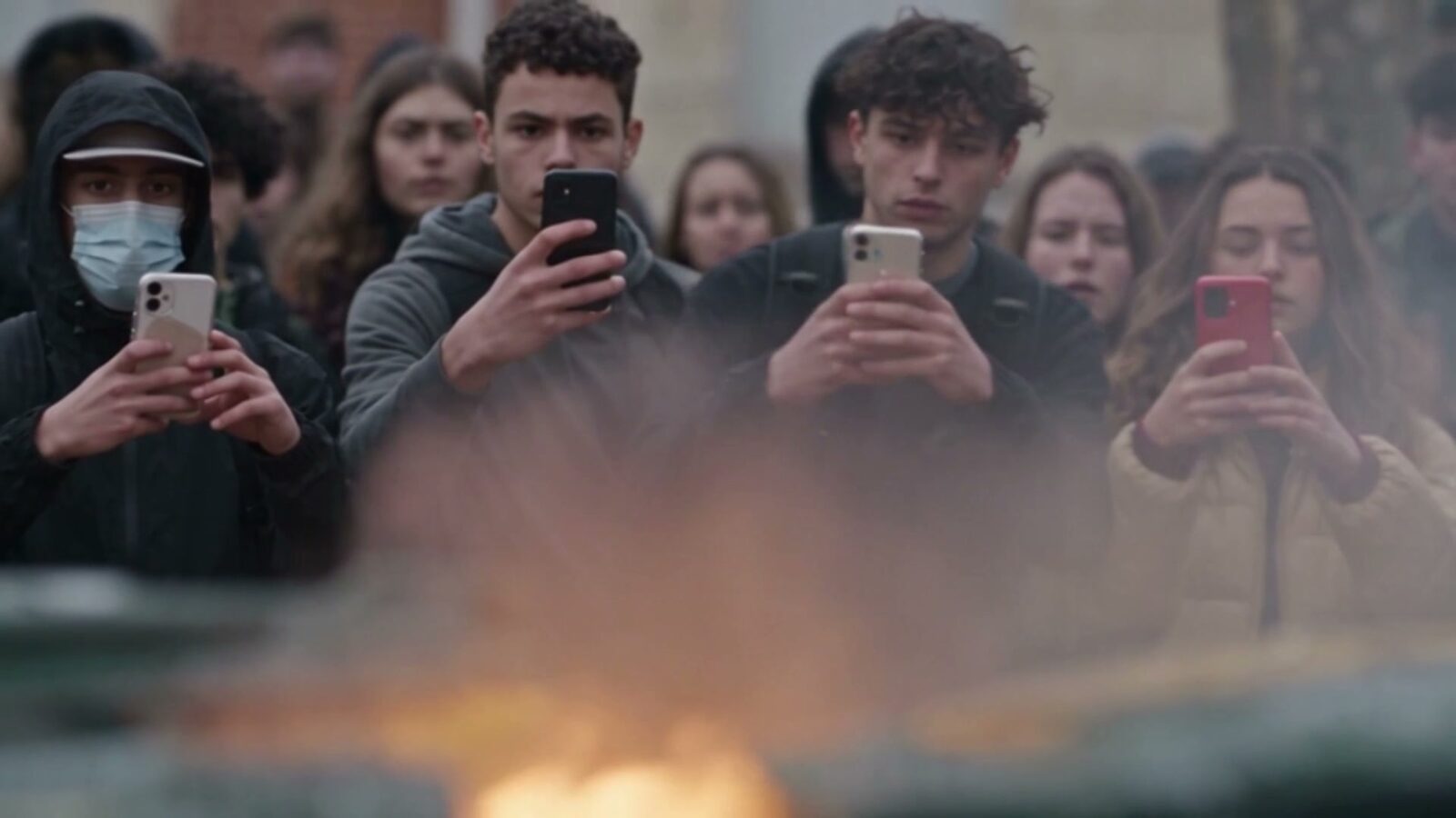 Des lycéens filment avec leur téléphone un feu qui brûle au premier plan