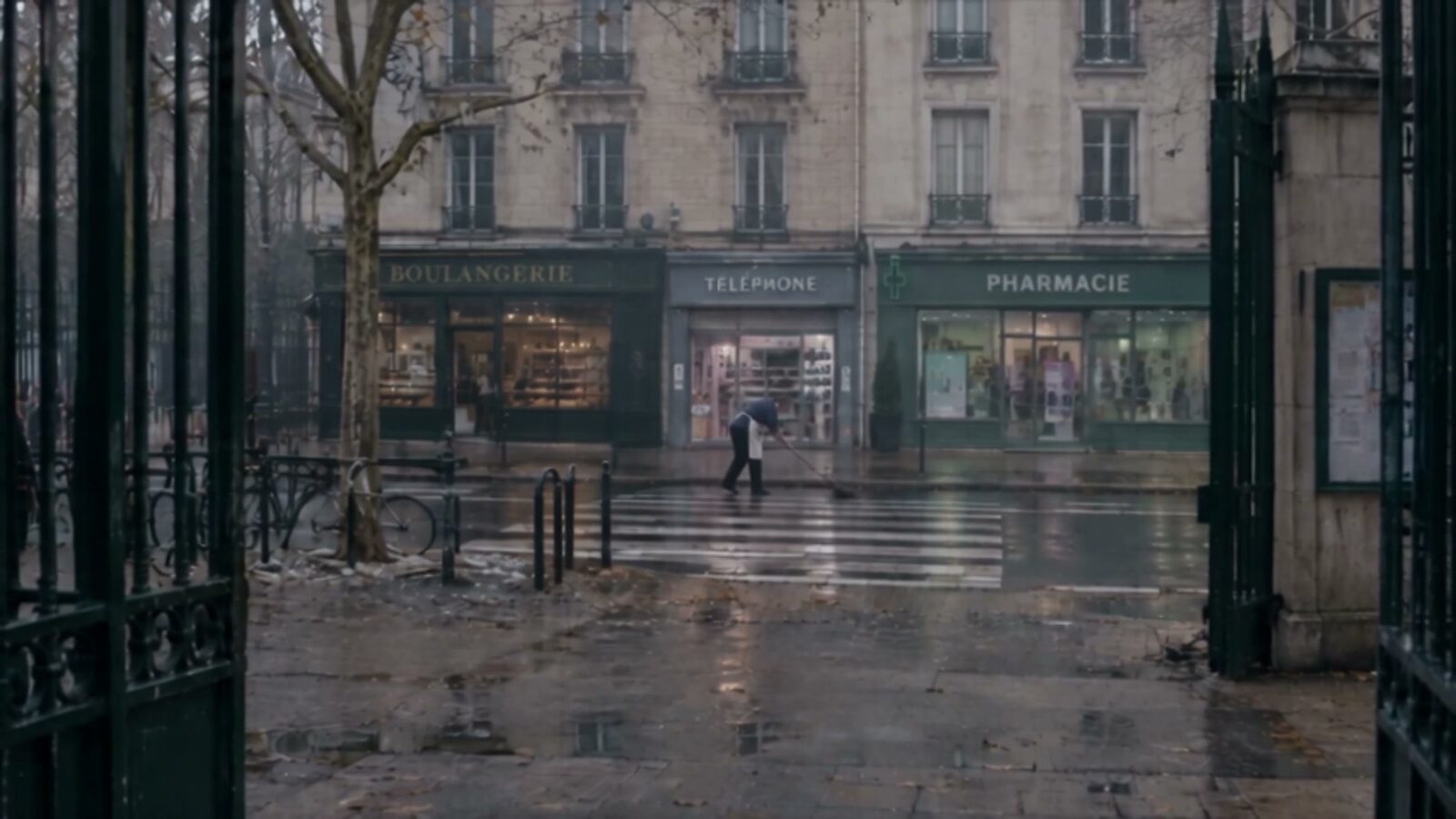 La rue vidée sous la pluie, vue à travers les grilles du lycée
